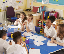 A group of primary school students working together at a table in a classroom.