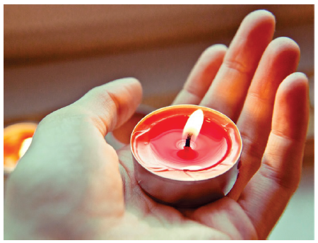 Image is a close-up of a hand holding a tea-light candle.