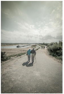 Image shows an eldery couple walking along a shoreline.