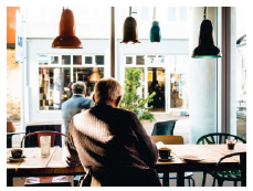 Image is of a man sitting in a cafe with his back to the camera.