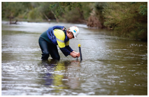 Photo shows a man testing water in a river.
