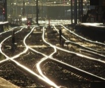 Multiple rows of metal railway tracks glowing in the sun. There are signals and other train infrastructure in the background.