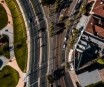 Birds-eye view of railway tracks and a major road near urban housing.