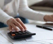 Close up of a person's hand using a calculator. The calculator sits on top of documents on a desk.