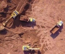 Aerial photo of yellow diggers and trucks preparing a cleared area for construction. The ground around the vehicles is brown dirt.
