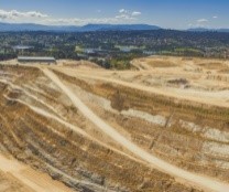 Wide aerial photo of a closed limestone mine in Melbourne. There are suburban houses and a mountain range in the background.