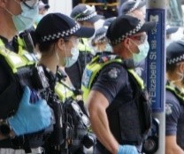 A group of Victoria Police officers on duty wearing PPE outside on a busy street.