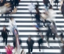 Aerial photo of pedestrians walking on a zebra crossing. The pedestrians are blurred and out of focus.