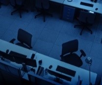 Overhead photo of two rows of empty desks in a dark office.