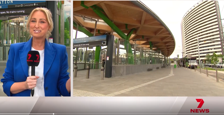 Screenshot of a 7 News television broadcast. On the left side is a reporter with a microphone standing outside Anzac station. On the right side is a photo of the exterior of Anzac Station. 