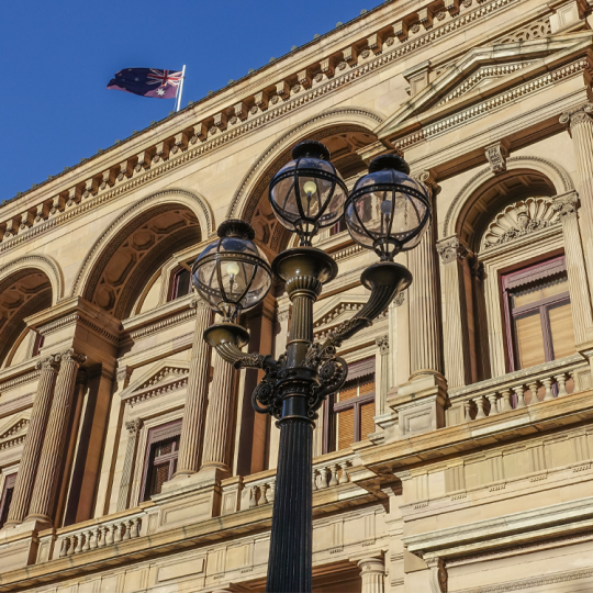 A Victorian-era lamp post outside the Parliament of Victoria. The Australian flag is in the background flying over the roof. 