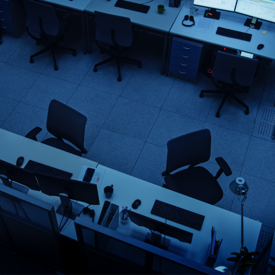 Overhead photo of two rows of empty desks in a dark office.