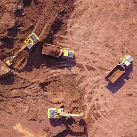 Aerial photo of yellow diggers and trucks preparing a cleared area for construction. The ground around the vehicles is brown dirt.