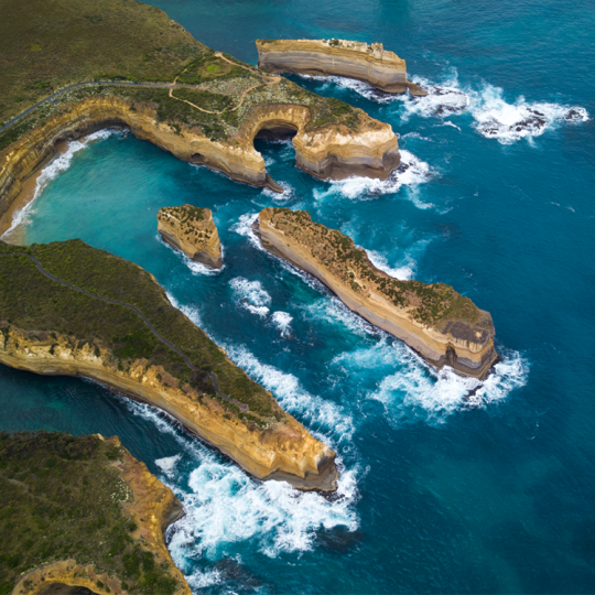 An aerial photo of the rugged Victorian coastline. The cliffs are eroding and forming small islands in the surf.