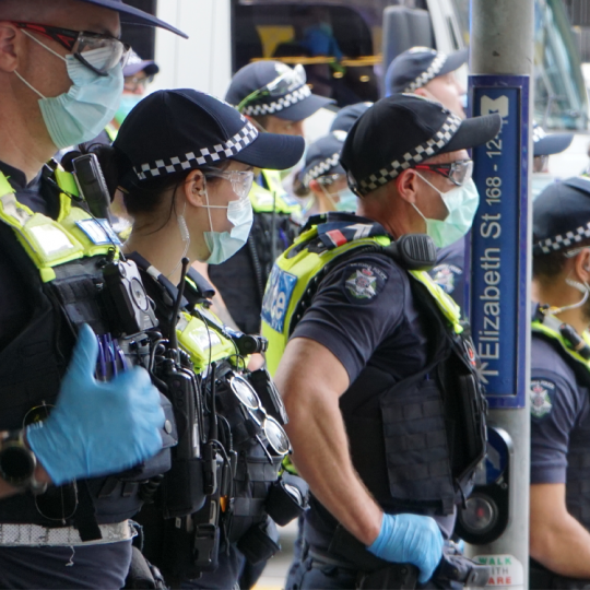 A group of Victoria Police officers on duty wearing PPE outside on a busy street.