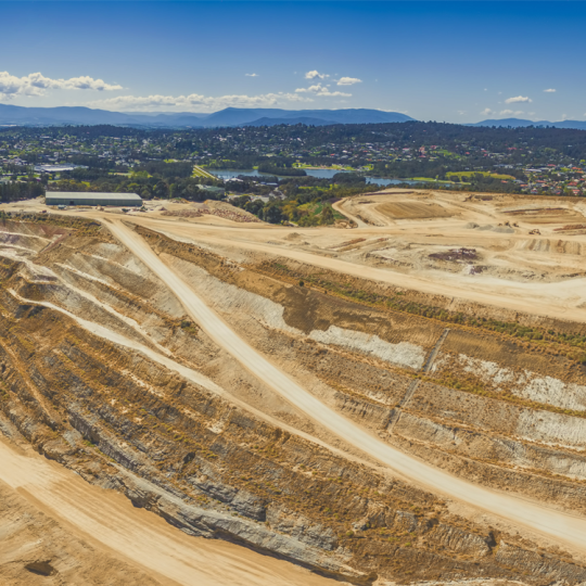 Wide aerial photo of a closed limestone mine in Melbourne. There are suburban houses and a mountain range in the background.