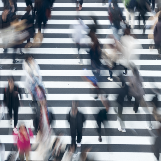 An aerial photo of pedestrians walking on a zebra crossing. The pedestrians are blurred and out of focus.