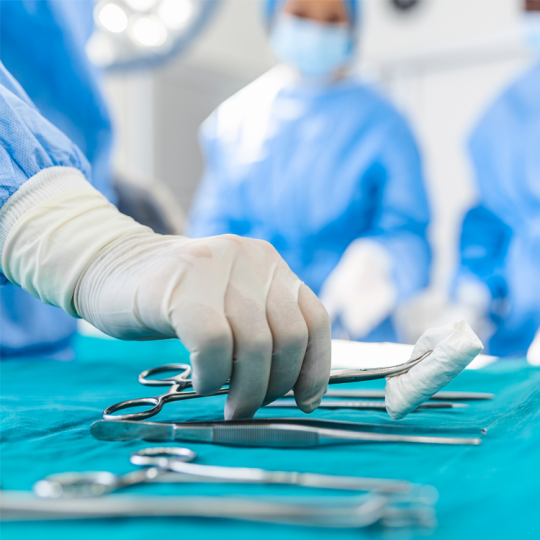Close-up of a nurse wearing surgical gloves reaching for a surgical instrument.