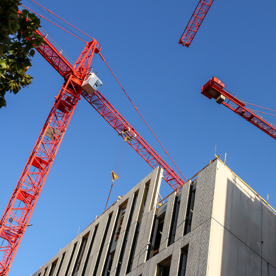 Red cranes against a blue sky on a construction site.