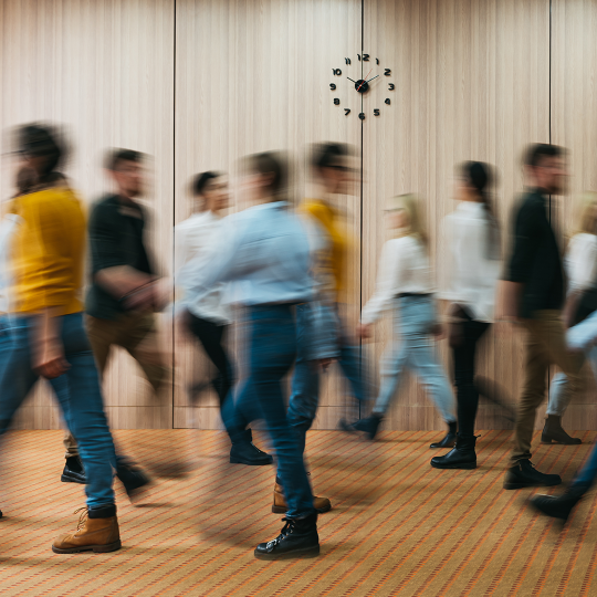 Nine blurred people in professional clothes walking through an office