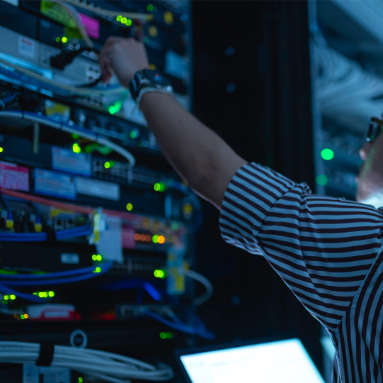 Close-up of an IT worker adjusting a cable in a server room. 