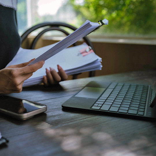 A person looking at papers with a laptop on the desk
