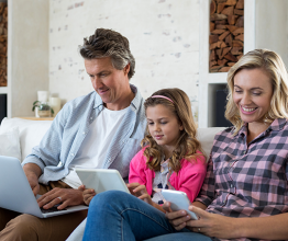 Family using laptop, digital tablet and mobile phone in living room at home. Photo courtesy of wavebreakmedia/Shutterstock.com