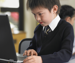 Young schoolboy using laptop at desk with girl in foreground. Photo courtesy of sirtravelalot/Shutterstock.com
