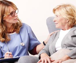 Portrait of home caregiver holding in hand a clipboard while sitting at living room near senior woman. Photo courtesy of Kinga/Shutterstock.com 