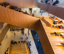 Overhead photo inside a university building. There are students mingling and walking up a large staircase. 