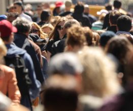 Dense crowd of people walking on a bright public street.