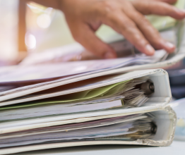 A close up image of a person's hand reaching for two binders filled with documents.