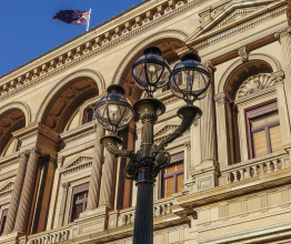 A Victorian-era lamp post outside the Parliament of Victoria. The Australian flag is in the background flying over the roof. 