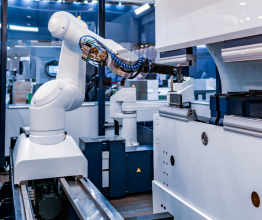 A white robotic arm in a modern industrial lab manufacturing something small in an automated production cell. 