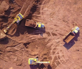 Aerial photo of yellow diggers and trucks preparing a cleared area for construction. The ground around the vehicles is brown dirt.
