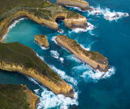 An aerial photo of the rugged Victorian coastline. The cliffs are eroding and forming small islands in the surf.