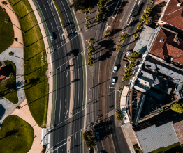 Birds-eye view of railway tracks and major road near urban housing.