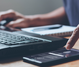 Close-up of a person's hand using multi-factor authentication on a phone to log in on a laptop.