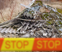 A pile of asbestos dumped in the environment. There is orange and yellow tape around it that says 'STOP'.