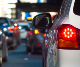 Close-up of a white car's tail light. The car is stopped in traffic on a busy road.