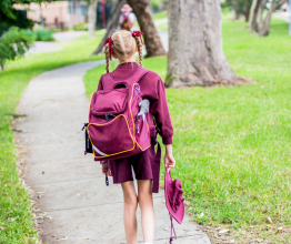 A primary school student in school uniform walking through a park to school.