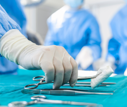 Close-up of a nurse wearing surgical gloves reaching for a surgical instrument.