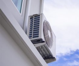 An air conditioner compressor unit on the side of a house on a sunny day.