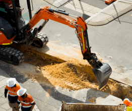 Excavator digging into a road with construction workers around