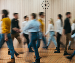 Nine blurred people in professional clothes walking through an office