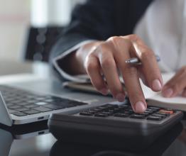 A woman's hand using a calculator while a laptop is open.